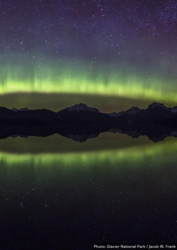 A night time view of mountains and green aurora across a lake.