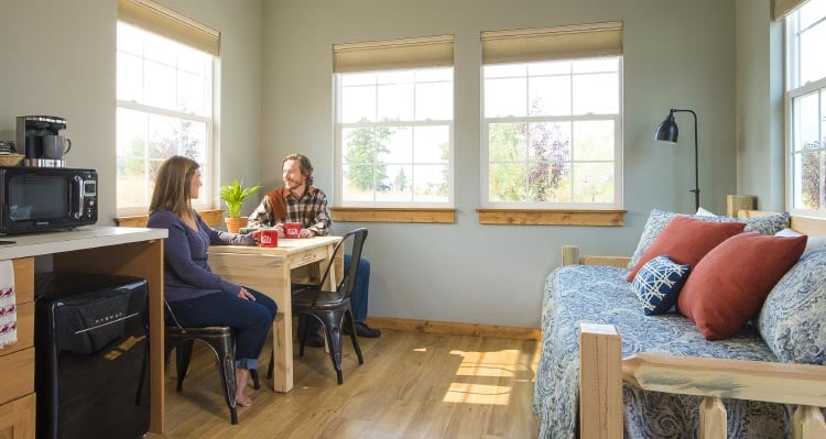 Two people sit at a table in a sun-lit room.