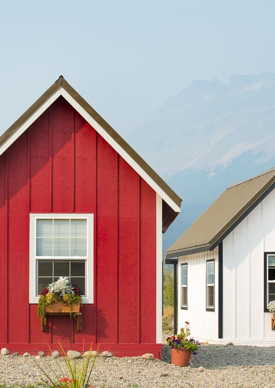 A red and white tiny home are surrounded by planters of flowers.