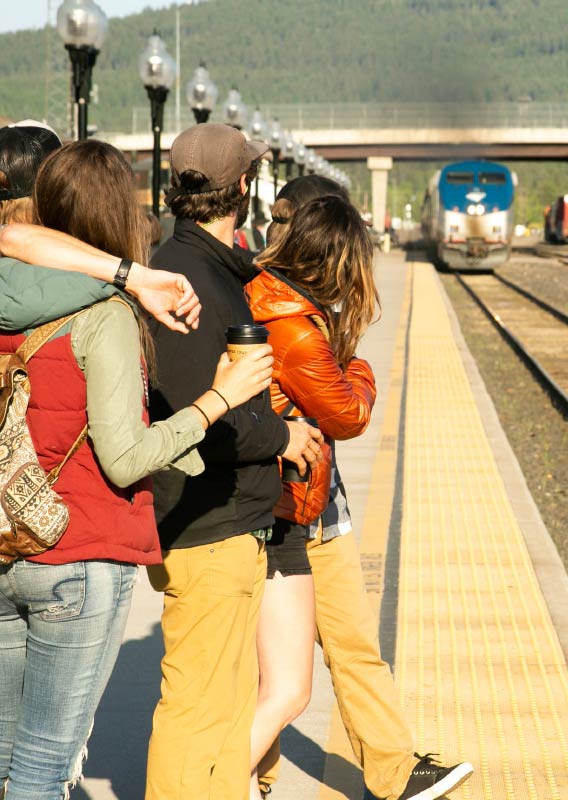 A group of people wait for the train to arrive at a platform.