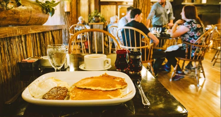 A breakfast plate of pancakes, eggs and sausage in a rustic dining room.