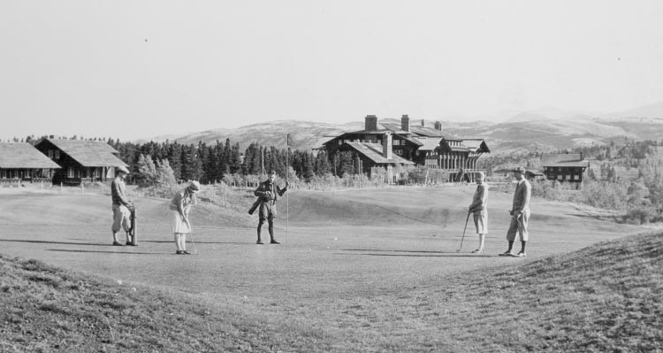 A group of people golf near a large lodge