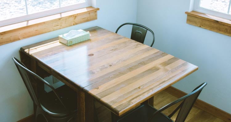 A table with three chairs underneath a sunny window.