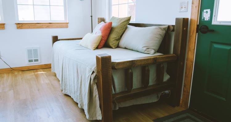 A wooden-frame bed up against a wall with the sun shining into a room.