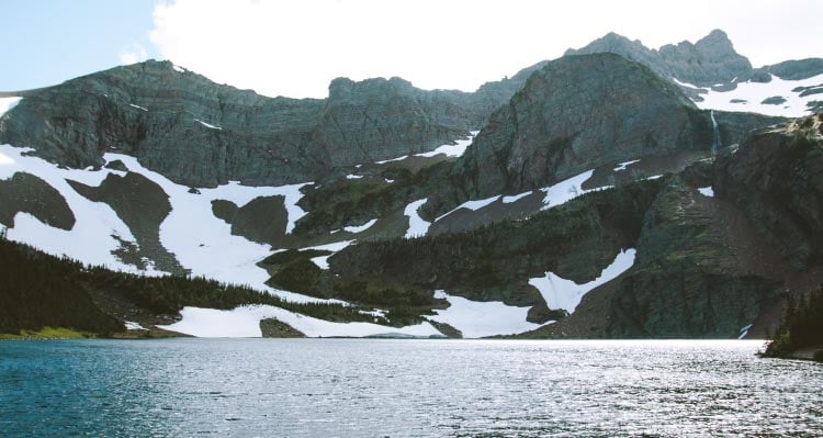 A view across a lake towards towering craggy mountains.