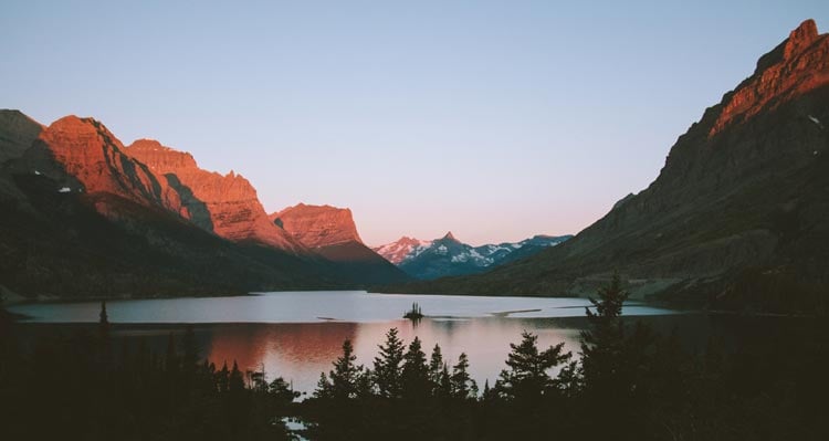 An island sits at the center of a long lake between mountains.