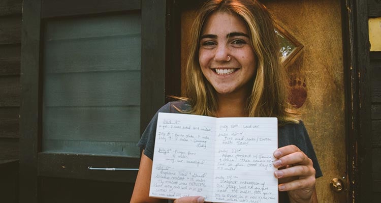 A woman holds up her hiking log in a small notebook.