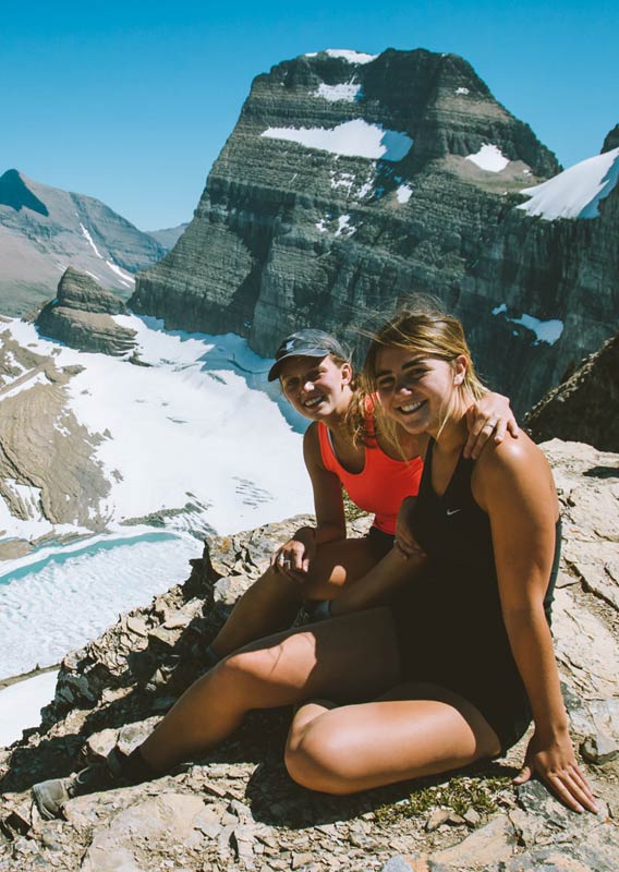 Two women sit on a rocky outcropping high among snow-covered mountains