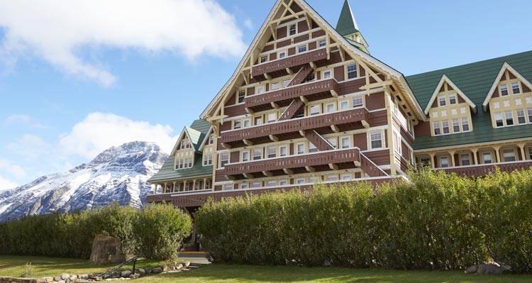 The Prince of Wales Hotel, with a gabled green roof with snow covered mountains behind.