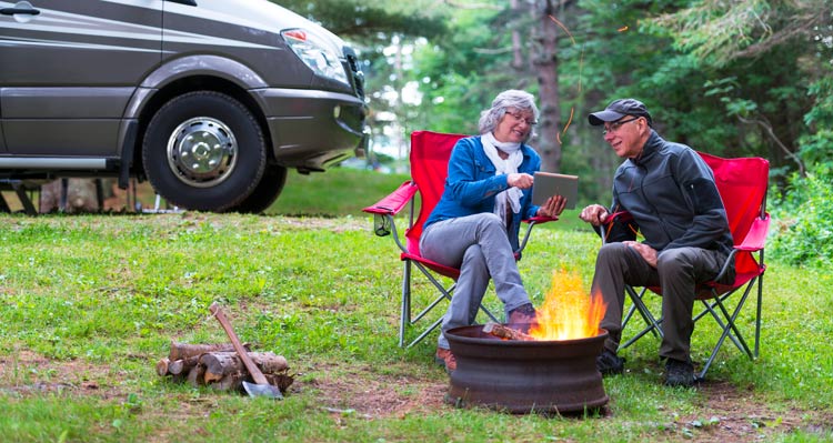 Two campers sit in chairs around a campfire.