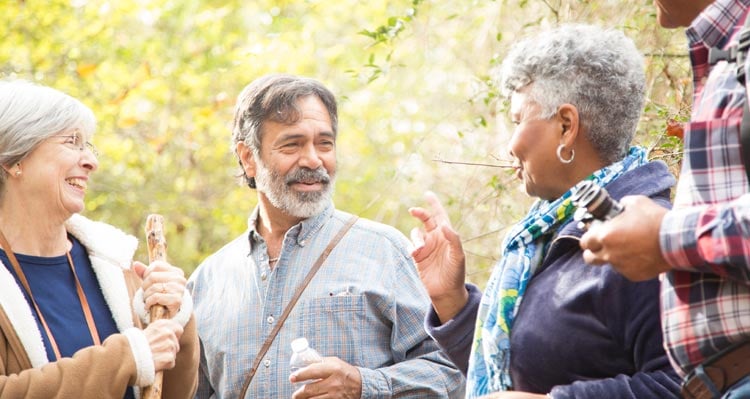 A group of people smile and chat on a forested trail.