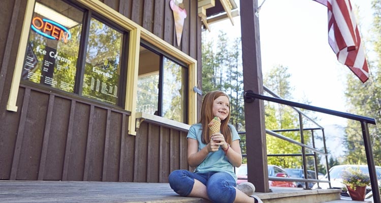A child smiles and holds an ice cream cone on a wooden stoop.
