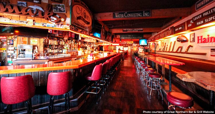 A long bar with stools and tables on the inside of the Great Northern Bar & Grill.