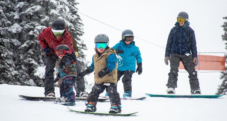 Three kids get ready to snowboard with their parents.