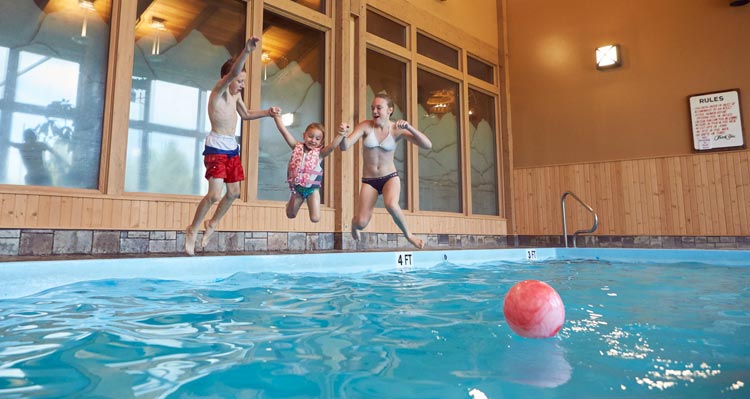 3 kids jump into an indoor swimming pool