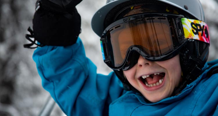 A young child dressed up in snow gear smiles widely.