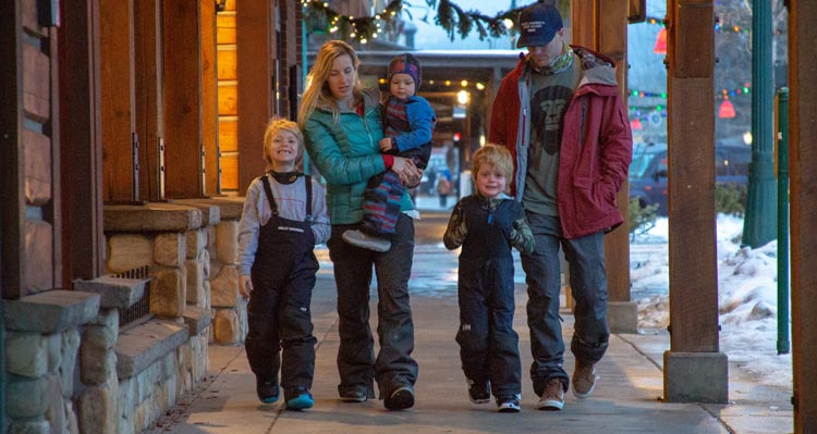 A family of five walk alongside shops under an awning in downtown Whitefish.