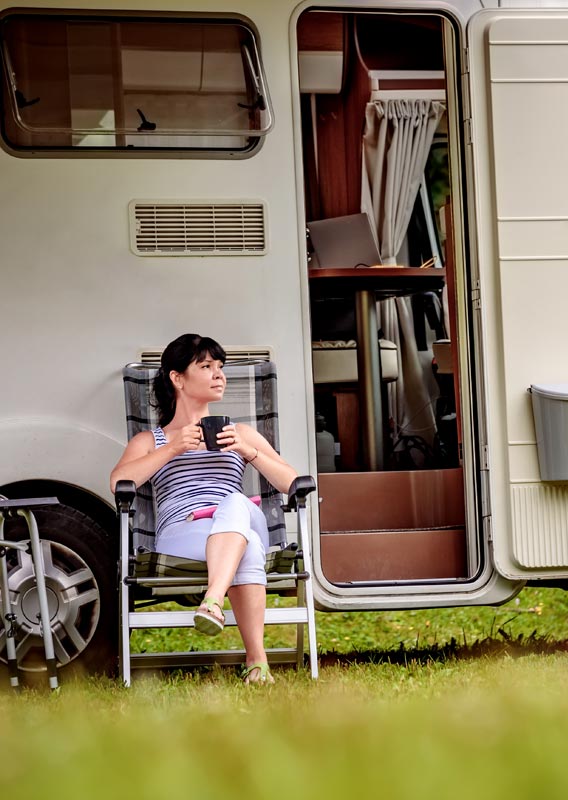 A woman sits outside an RV with a cup of coffee.