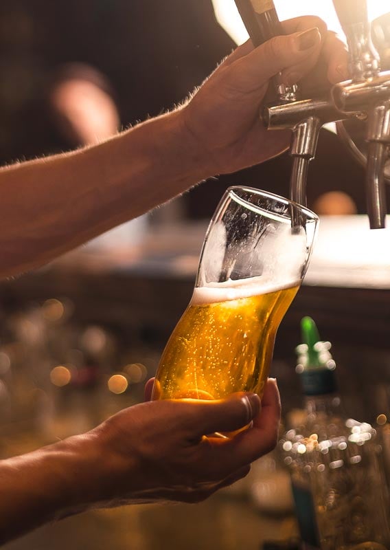 A bartender pours a pint of beer from a draft tap.