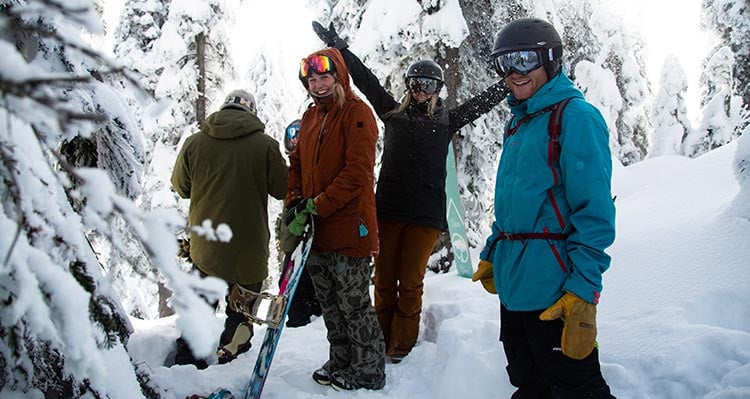 Friends take a break on the ski hill between snow-covered trees.