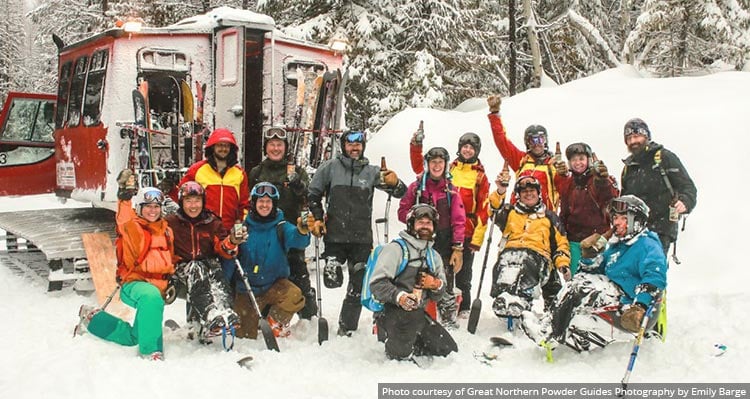 A group of skiiers gather around a snowcat near a wintry forest