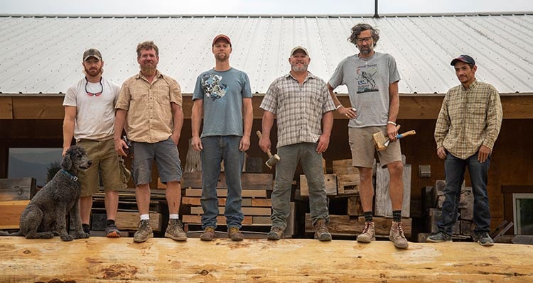 A team of wordworkers stand atop a large timber.