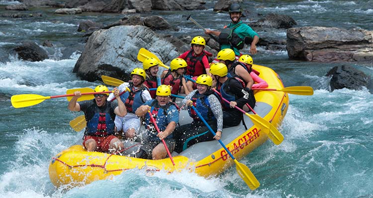 A group of people in a raft as it goes down the river, the guide in the back is standing