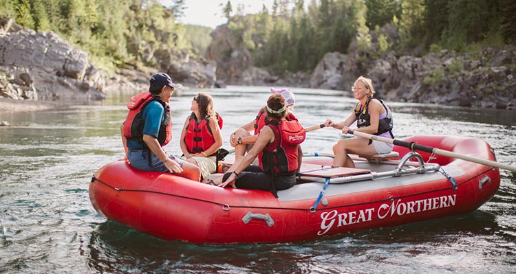 Five people sit and paddle a red raft.