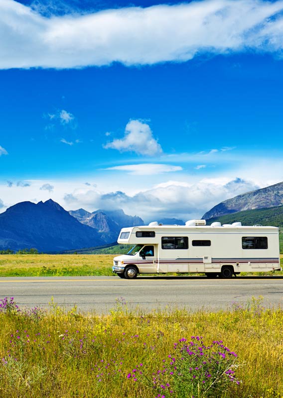 An RV drives along a road on an open plain near mountains.