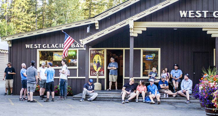 A crowd of people standing and sitting around a wooden tavern