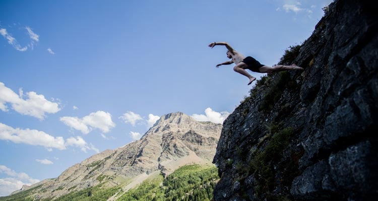 A man jumps from a cliffside into a lake.