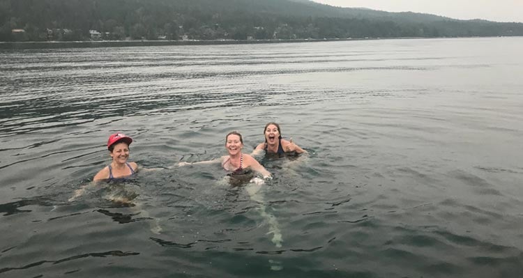 Three people smile while swimming in a lake.