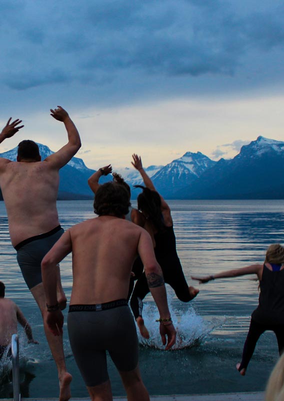 A group of people jump into a lake surrounded by mountains