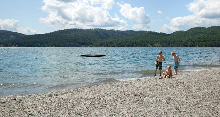 Three children play on a pebble beach near a lake shore.