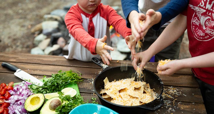 A family puts shredded cheese on to a plate of nachos.