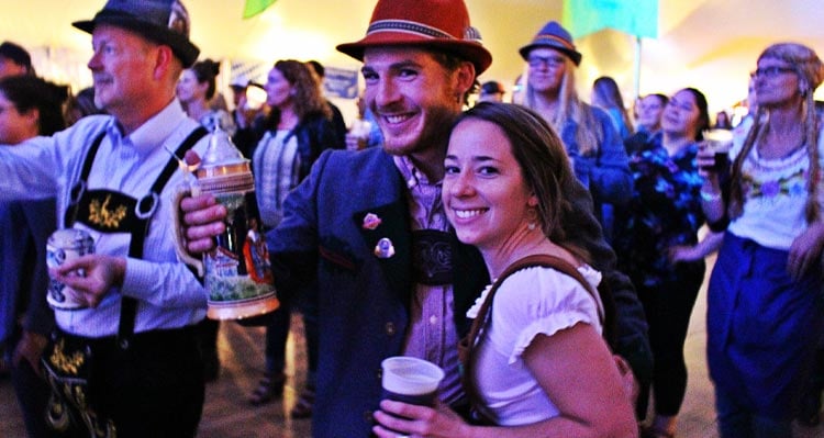 Two people celebrate Oktoberfest in a crowd of other people also celebrating and dancing.