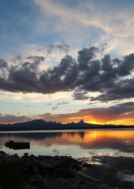 An orange sunset behind a mountain horizon across a calm lake.