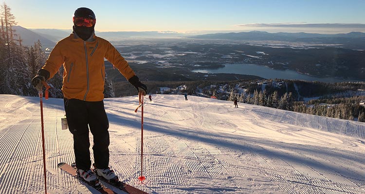 A skier in a yellow jacket at the top of a ski hill.