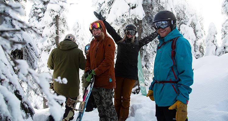 A group of friends in ski gear stand among snow-covered trees