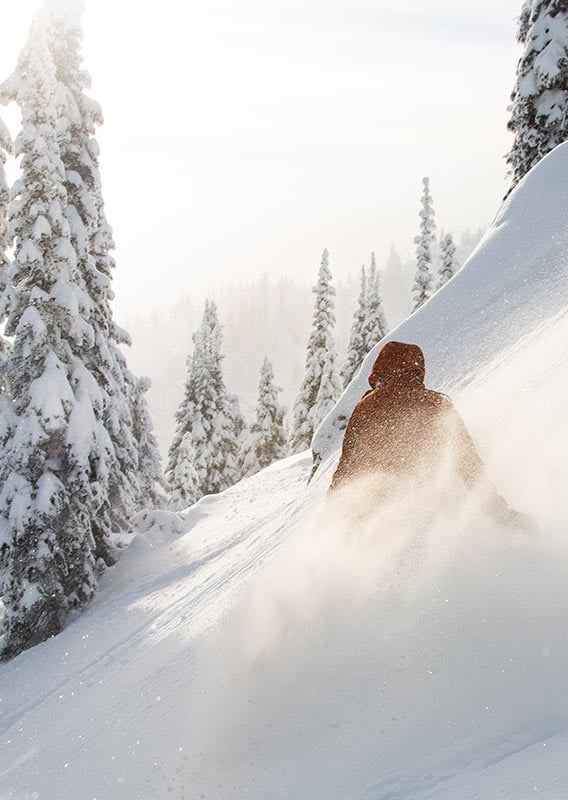 A skier makes their way down a steep slope with powder snow all around.