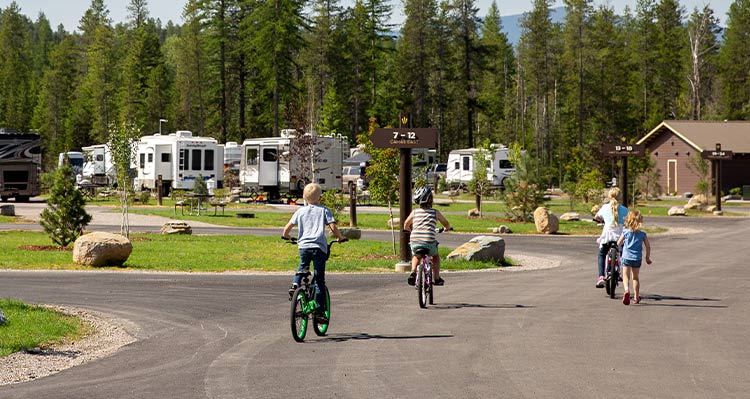 A group of kids ride their bikes through an RV park.