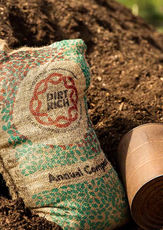 A burlap bag of compost lays against a rusted can and pile of compost