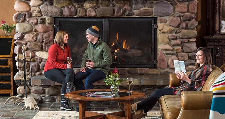 Two people sit next to a fireplace and another sits on a lounge couch.