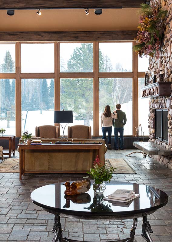 Two people stand at a big window in a hotel lobby looking out to a snowy landscape.