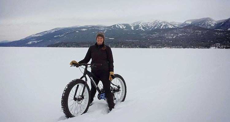 A person stands with their bicycle on a snowy frozen lake.