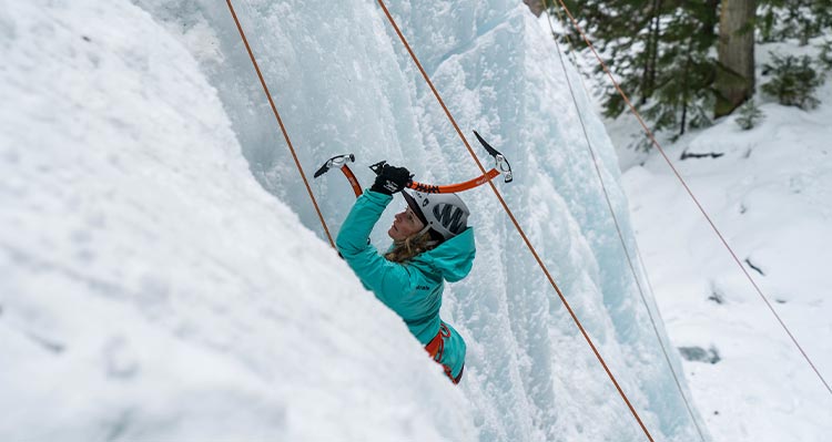 An ice climber ascends a frozen waterfall, secured with ropes.