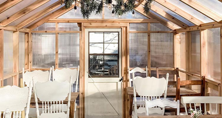 A small greenhouse with four sets of antique tables and chairs for dining.