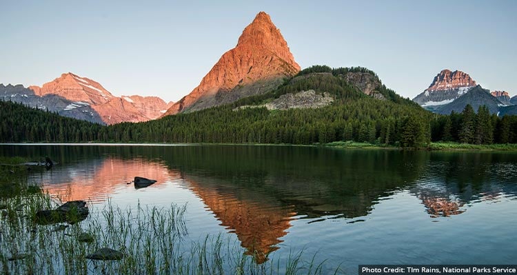 A mountain range reflects into the lake at sunset.