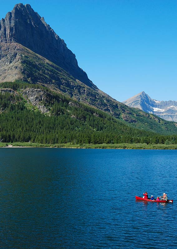 A family in a red canoe paddles across the lake. Mountains behind.