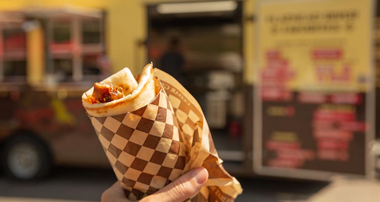 A food wrap with meat in it, being held outside of a food truck.